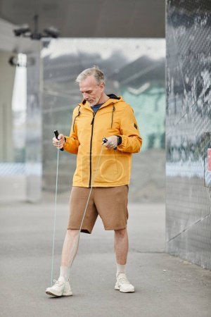 Photo for Vertical portrait of handsome mature man exercising outdoors with skipping rope in urban city setting - Royalty Free Image
