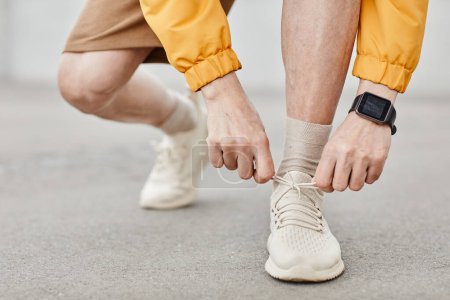 Foto de Primer plano mínimo de hombre irreconocible atando cordones de zapatos durante la carrera al aire libre, espacio de copia - Imagen libre de derechos