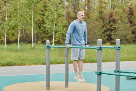 Photo for Full length portrait of sportive mature man exercising on parallel bars during outdoor workout, copy space - Royalty Free Image