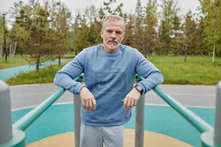 Photo for Waist up portrait of active mature man exercising on parallel bars outdoors and looking at camera, copy space - Royalty Free Image
