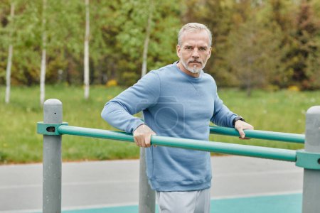 Photo for Waist up portrait of handsome mature man exercising on parallel bars during outdoor workout and looking at camera, copy space - Royalty Free Image