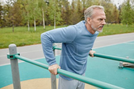 Photo for Side view portrait of active mature man exercising on parallel bars outdoors, copy space - Royalty Free Image