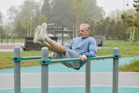 Foto de Retrato completo del hombre maduro deportivo ejercitándose en barras paralelas al aire libre, espacio de copia - Imagen libre de derechos