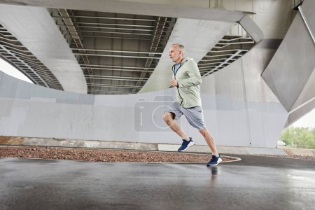 Photo for Motion shot of active mature man running against concrete background in urban city setting, copy space - Royalty Free Image