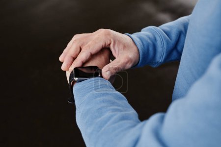 Téléchargez les photos : Gros plan d'un homme méconnaissable mettant en place smartwatch sur fond noir, espace de copie - en image libre de droit