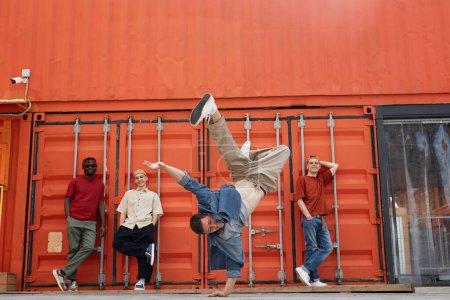 Photo for Motion shot of all male dance team performing hip-hop and breakdance in urban city setting, focus on man doing handstand pose - Royalty Free Image