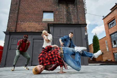 Foto de Motion shot de un joven haciendo poses de breakdance al aire libre con todo el equipo de baile masculino en el fondo - Imagen libre de derechos