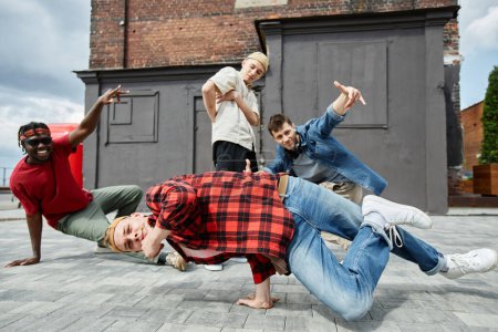 Téléchargez les photos : Motion shot de jeune homme faisant handstand pose à l'extérieur avec toute l'équipe de breakdance masculine en arrière-plan - en image libre de droit