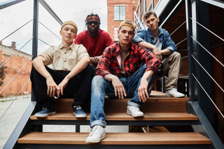 Photo for Diverse group of boys wearing street fashion while posing on metal stairs in urban setting - Royalty Free Image