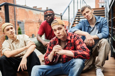 Photo for Diverse group of young guys wearing street fashion while posing on metal stairs in urban setting - Royalty Free Image