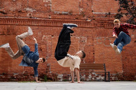 Photo for Freeze frame of all male breakdancing team jumping in air against brick wall outdoors - Royalty Free Image