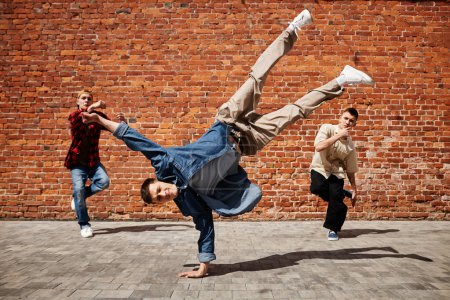 Foto de Congelar el marco del intérprete de breakdance masculino haciendo pose de mano con el equipo contra la pared de ladrillo al aire libre - Imagen libre de derechos