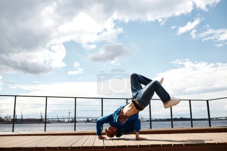 Téléchargez les photos : Prise de vue complète du danseur hip-hop masculin posant à l'extérieur et faisant la main contre le ciel, espace de copie - en image libre de droit