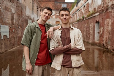 Foto de Cintura neutra hacia arriba retrato de dos chicos gemelos mirando a la cámara en un entorno urbano deprimente con paredes de ladrillo - Imagen libre de derechos