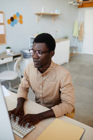 Téléchargez les photos : Portrait vertical de jeune développeur de logiciels noirs utilisant un ordinateur tout en travaillant dans un bureau informatique - en image libre de droit