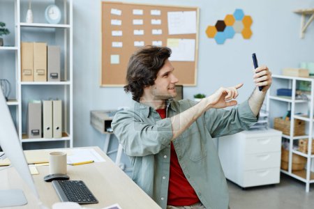 Photo for Side view portrait of Caucasian young man taking selfie photo at workplace in office - Royalty Free Image