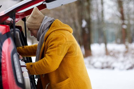 Foto de Retrato de vista lateral del hombre abriendo el maletero en invierno mientras viaja por vacaciones, espacio para copiar - Imagen libre de derechos