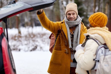 Photo for Portrait of smiling young couple opening car trunk in winter while travelling for holidays, copy space - Royalty Free Image