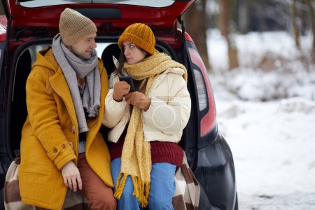 Photo for Portrait of young couple sitting in car trunk in winter forest while enjoying travel for holidays, copy space - Royalty Free Image