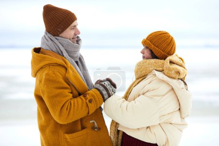 Téléchargez les photos : Vue de côté portrait de romantique jeune couple tenant la main dans le paysage d'hiver, sortir ensemble ou concept de proposition - en image libre de droit