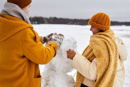 Téléchargez les photos : Gros plan de jeune couple construisant bonhomme de neige ensemble tout en profitant du plaisir hivernal en plein air - en image libre de droit