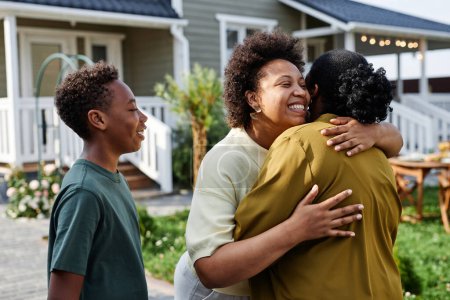 Téléchargez les photos : Portrait taille haute de la famille afro-américaine embrassant tout en accueillant les invités pour la fête d'été en plein air - en image libre de droit