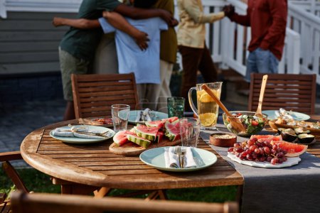 Téléchargez les photos : Image de fond de la table de pique-nique de fête à l'extérieur avec la famille noire célébrant en arrière-plan, espace de copie - en image libre de droit