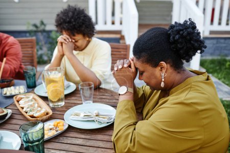 Foto de Retrato de una joven negra rezando en la mesa al aire libre durante la reunión familiar - Imagen libre de derechos