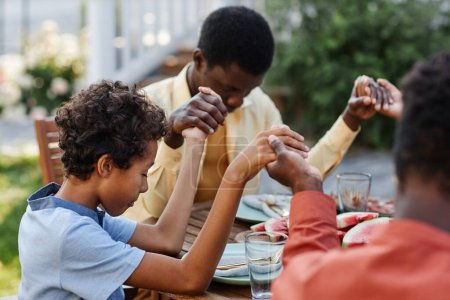 Photo for Portrait of young African American boy saying grace at table outdoors during family gathering and holding hands - Royalty Free Image