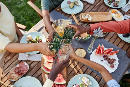 Foto de Vista superior en el grupo de personas afroamericanas tintineo vasos sobre la mesa con deliciosa comida al aire libre - Imagen libre de derechos
