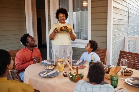 Foto de Retrato de una mujer negra mayor llevando comida a la mesa mientras disfruta de la reunión familiar al aire libre - Imagen libre de derechos