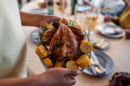 Téléchargez les photos : Gros plan d'une femme afro-américaine apportant un plat de poulet fait maison à table lors d'un rassemblement familial - en image libre de droit
