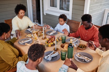 Foto de Retrato de la familia afroamericana diciendo gracia en la mesa de la cena y tomados de la mano en un ambiente acogedor por la noche - Imagen libre de derechos