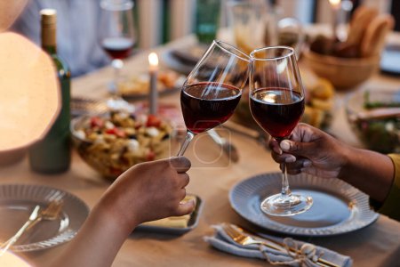 Foto de Primer plano de la familia tintineo copas de vino en la mesa de la cena al aire libre, ambiente acogedor por la noche - Imagen libre de derechos