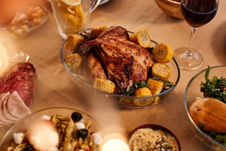 Photo for Close up of roasted chicken on dinner table with rustic homemade dishes in cozy setting - Royalty Free Image