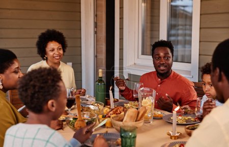 Téléchargez les photos : Portrait de femme afro-américaine souriante appréciant le dîner en famille sur la terrasse en plein air - en image libre de droit