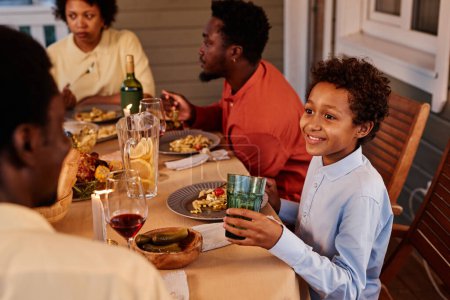 Foto de Retrato de niño afroamericano sonriente disfrutando de la cena con la familia en la terraza al aire libre - Imagen libre de derechos
