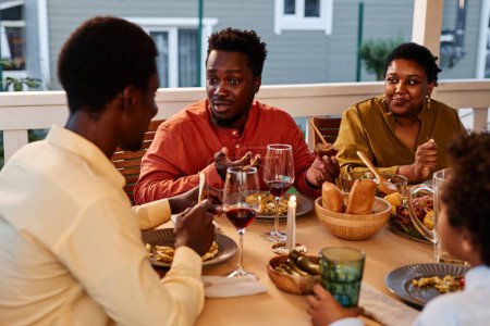 Foto de Retrato del joven negro hablando con la familia mientras disfrutan de la cena juntos en la terraza - Imagen libre de derechos