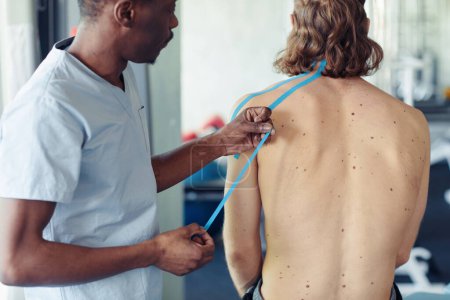 Téléchargez les photos : Thérapeute africain appliquant du ruban adhésif sur le dos au patient avant l'entraînement au gymnase - en image libre de droit