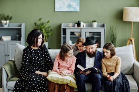 Téléchargez les photos : Portrait de famille juive avec trois enfants lisant ensemble un livre dans un cadre familial moderne - en image libre de droit
