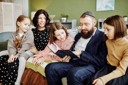 Téléchargez les photos : Portrait de l'homme juif orthodoxe portant kippah tout en lisant le livre à de nombreux enfants à la maison - en image libre de droit