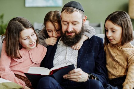 Porträt eines orthodoxen jüdischen Mannes, der Kippa trägt, während er drei Kindern ein Buch vorliest