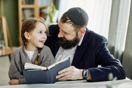 Téléchargez les photos : Portrait du père juif souriant lisant le livre avec sa fille à la maison - en image libre de droit