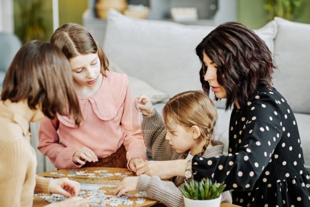 Téléchargez les photos : Portrait latéral de la jeune mère avec trois enfants jouant avec puzzle ensemble dans le cadre de la maison - en image libre de droit