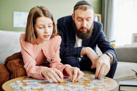 Téléchargez les photos : Portrait de père juif orthodoxe jouant à un jeu de puzzle avec une jeune fille à la maison - en image libre de droit