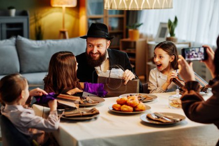 Téléchargez les photos : Portrait de la famille juive moderne partageant des cadeaux à table dans un cadre confortable - en image libre de droit