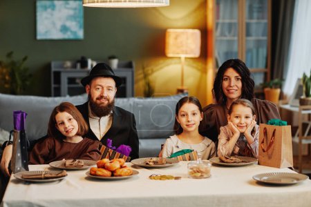 Téléchargez les photos : Portrait de la famille juive moderne regardant la caméra tout en étant assis à table dans un cadre confortable à la maison - en image libre de droit