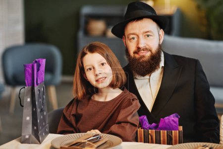Photo for Portrait of modern jewish man with daughter looking at camera while sitting at dinner table in cozy home setting - Royalty Free Image
