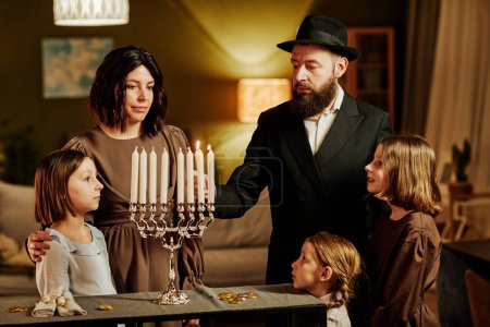 Foto de Retrato de la familia judía ortodoxa encendiendo la vela menorah durante la celebración de Hanukkah en casa - Imagen libre de derechos