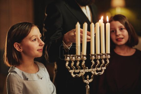 Foto de Retrato de vista lateral de una joven mirando la vela menorah durante las vacaciones de Hanukkah en un hogar judío - Imagen libre de derechos